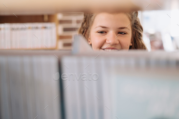 Teenager girl picking a book on a library shelf / Photodune, Misc