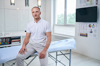 Handsome Caucasian chiropractor sitting on massage table in medical office / Photodune, Misc