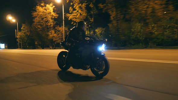 Young Man in Helmet Riding Fast on Modern Black Sport Motorbike at Evening City Street