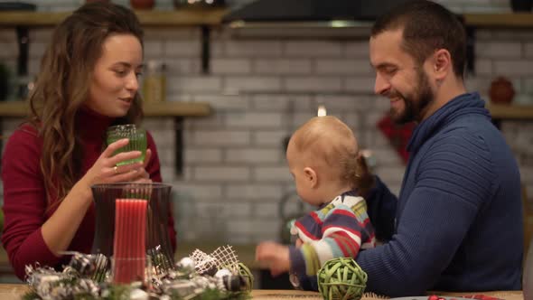 Portrait of Mother, Father and a Baby Sitting at the Table in Modern Kitchen