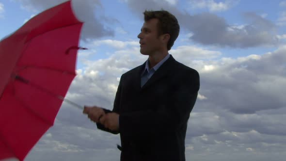 Cu of a male opening an umbrella on a beach and checking if it is raining