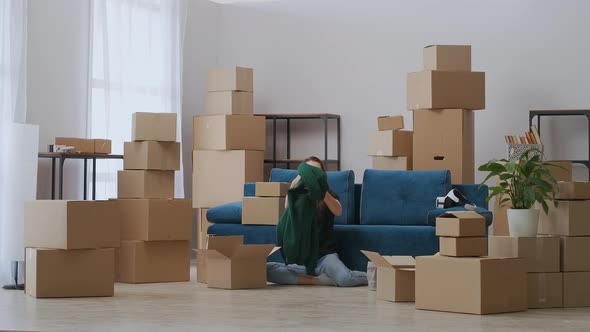 A Young Girl is Sitting on the Floor Near the Sofa Packing for the Move