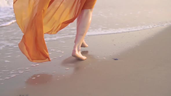 Female Bare Feet and Fluttering Dress at Sunset. Young Barefoot Girlrunning in Long Orage Dress