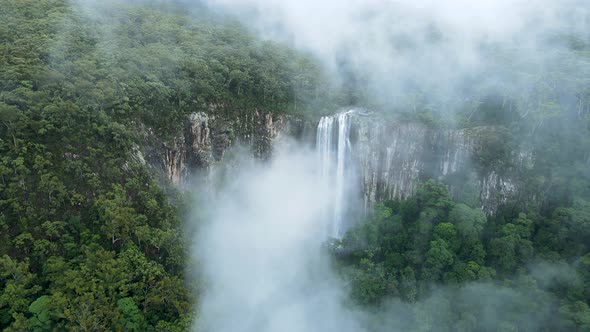 Looking through a mist covered mountain revealing a majestic waterfall descending into a tropical ra