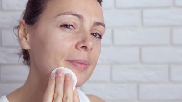 Woman wipe her face with a cotton pad.