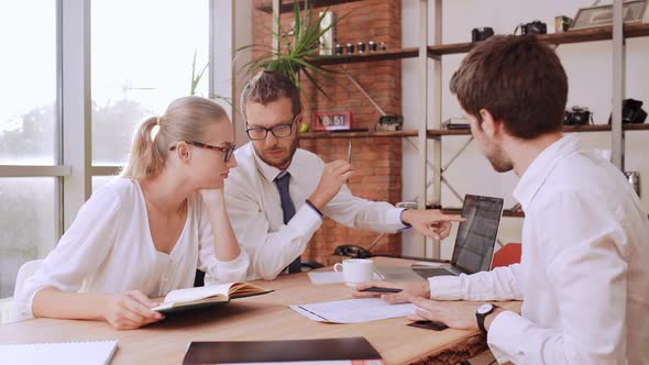 Thre Female and Male Office Workers in White Shirts and Glasses Sitting at Table Discussing Project