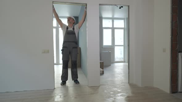 A Builder in Working Uniform Checks the Size and Quality of Doorways in a New Apartment