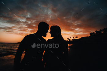 Romantic couple on the beach in a colorful sunset in the background.A guy and a girl at sunset on / Photodune, Misc