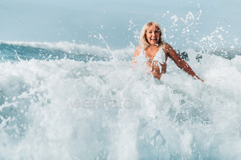 A girl with wet hair jumps over large waves in the Atlantic ocean, around a wave with splashes of / Photodune, Misc