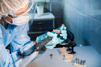 A masked and gloved dental technician works on a prosthetic tooth in his lab / Photodune, Misc