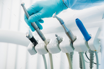 a dentist wearing gloves in the dental office holds a tool before working / Photodune, Misc