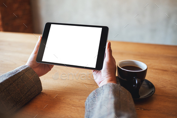 woman holding black tablet pc with blank white screen with coffee cup on wooden table / Photodune, Misc