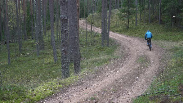 Man Biker is Riding Bicycle Along Rural Ground Road in Forest Back View