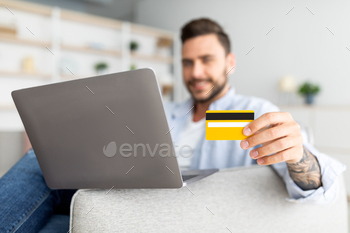 laptop and credit card sitting on sofa, selective focus. Positive guy enjoying making payments from home