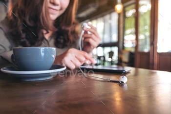 Closeup image of a woman holding earphones while listening to music with mobile phone  in cafe / Photodune, Misc