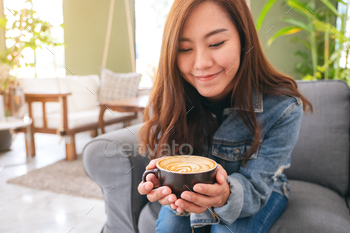 Closeup image of a beautiful asian woman holding and drinking hot coffee in cafe / Photodune, Misc