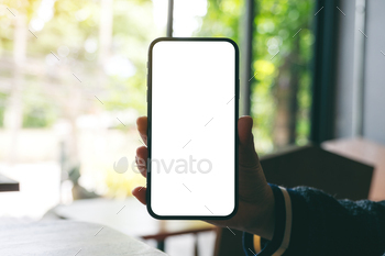Mockup image of a hand holding and showing black mobile phone with blank screen in cafe / Photodune, Misc