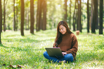 A beautiful asian woman working and typing on laptop keyboard while sitting in the park / Photodune, Misc