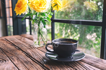 Closeup image of a black cup of hot coffee and yellow roses in a vase on vintage wooden table / Photodune, Misc