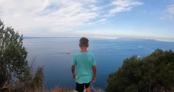 Back View of Young Boy Standing on Top of a Large Stone Rock Having a Panoramic View Adriatic sea