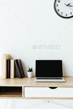 laptop with blank screen and books on work desk in front of white wall / Photodune, Misc