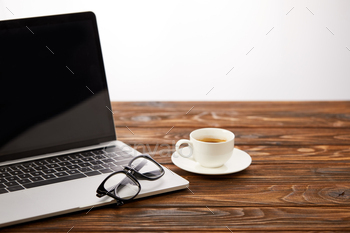 laptop with blank screen, eyeglasses and cup of coffee on wooden surface / Photodune, Misc