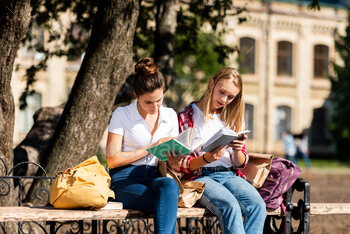 teen schoolgirls sitting on bench and doing homework together / Photodune, Misc