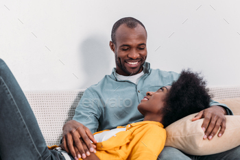 african american girlfriend lying on boyfriends legs on sofa at home / Photodune, Misc