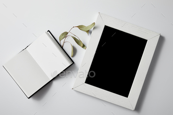 top view of opened notebook with green leaves and blank frame on white surface for mockup / Photodune, Misc
