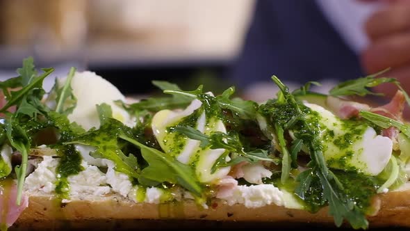 male chef pours olive oil over large sandwich with cheese cucumber ham and salad