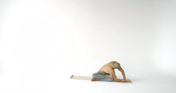 Male Yogi Is Training Alone in White Studio, Stretching His Muscles, Leaning His Torso