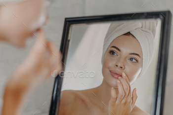 Woman wears minimal makeup, takes care of complexion and lips, looks at herself in mirror / Photodune, Misc