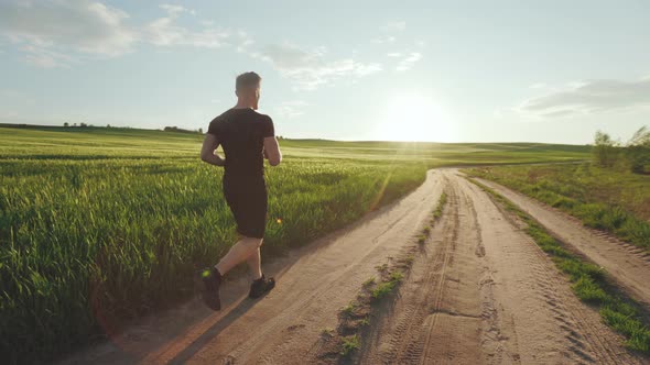 A Sporty Man is Running Along a Dirt Road Near a Field