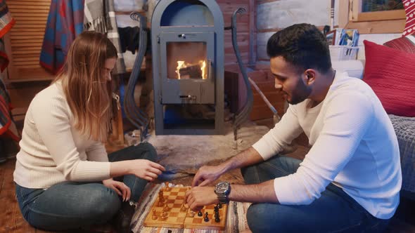Young Multiracial Couple Playing Chess Near the Fireplace in Cozy Home