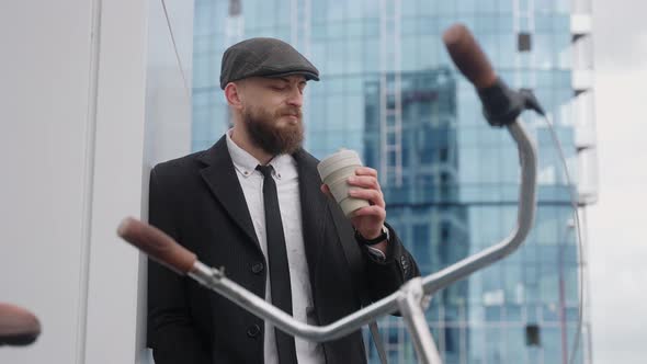 A Man Drinks Coffee in a Suit and Hat Near a Business Center