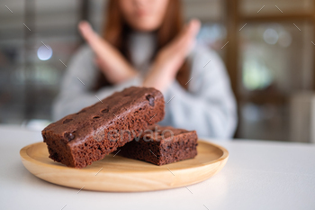 A woman making arms cross sign to refuse a brownie cake in wooden plate / Photodune, Misc