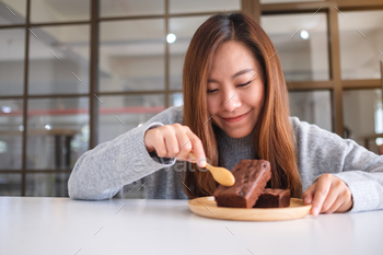 Closeup image of a beautiful asian woman eating delicious brownie cake with spoon / Photodune, Misc