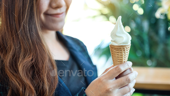 Closeup image of a woman holding and eating soft serve ice cream waffle cone / Photodune, Misc