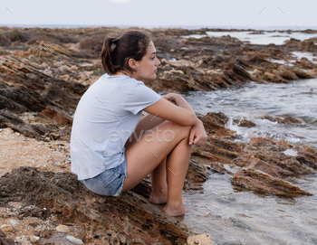 Teenage girl sitting on cliff by the sea / Photodune, Misc