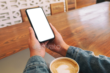 A woman holding black mobile phone with blank desktop screen with laptop and coffee cup on the table / Photodune, Misc