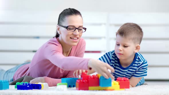 Smiling Woman Child Psychologist and Baby Boy Playing with Colorful Constructor Block Lying on Floor