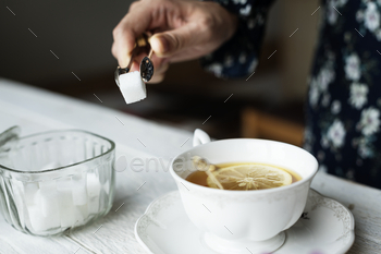 Woman helping herself with a sugar cube for her cup of nice hot lemon tea / Photodune, Misc