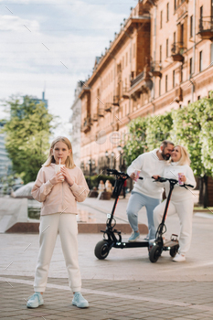 A girl with a drink in her hands is standing in the city and behind her on electric scooters are her / Photodune, Misc