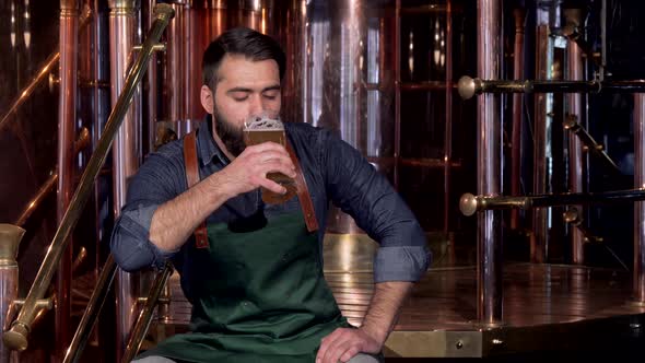 Cheerful Beer Maker Resting at His Brewery After Working, Drinking Delicious Beer