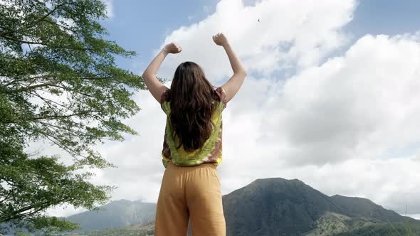 Girl with Long Hair in a Colored Tshirt and Yellow Trousers Stands and Raises Her Hands Up Against