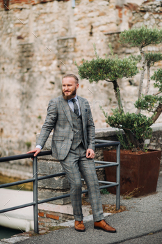 A man with a beard in a strict grey three-piece suit with a tie in the old town of Sirmione, a / Photodune, Misc