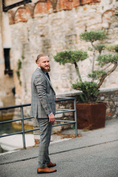 A man with a beard in a strict grey three-piece suit with a tie in the old town of Sirmione, a / Photodune, Misc