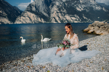 a girl in a smart white dress is sitting on the embankment of lake Garda.A woman is photographed / Photodune, Misc