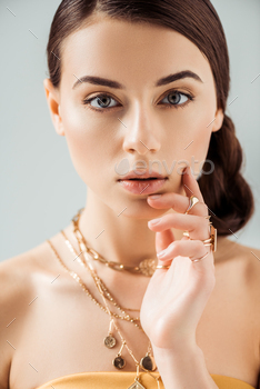 young woman with shiny makeup in golden necklaces and rings looking at camera isolated on grey / Photodune, Misc