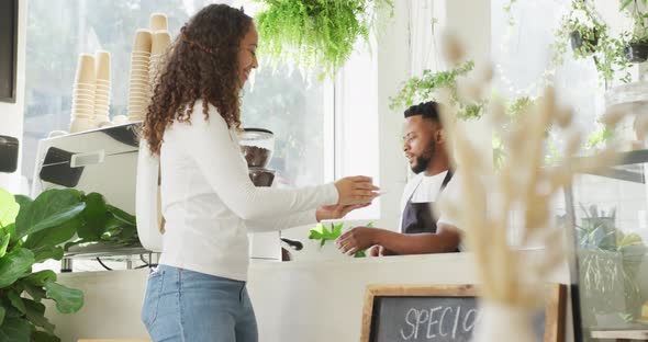 Happy african american male barista making coffee for biracial female client at cafe